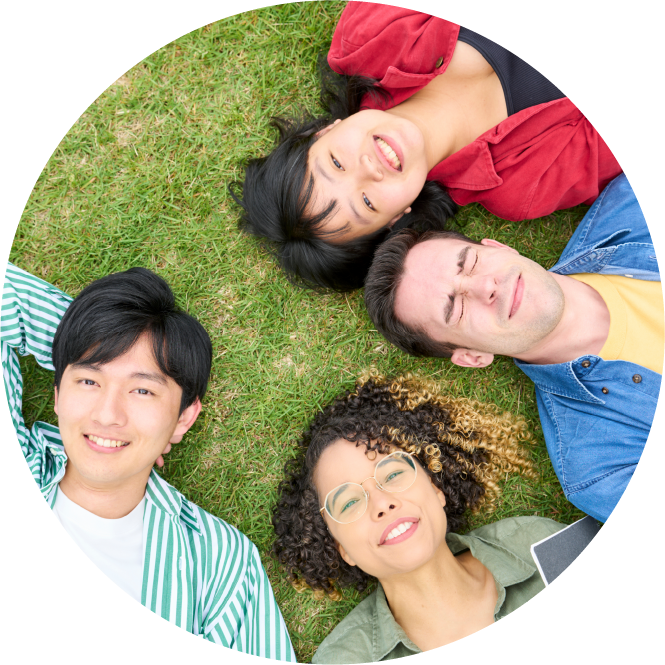 芝生で寝そべる4人の多国籍な大学生の写真